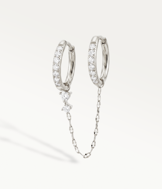 Two silver-tone Andromede hoop earrings with rhinestones, connected by a chain with a small pendant.