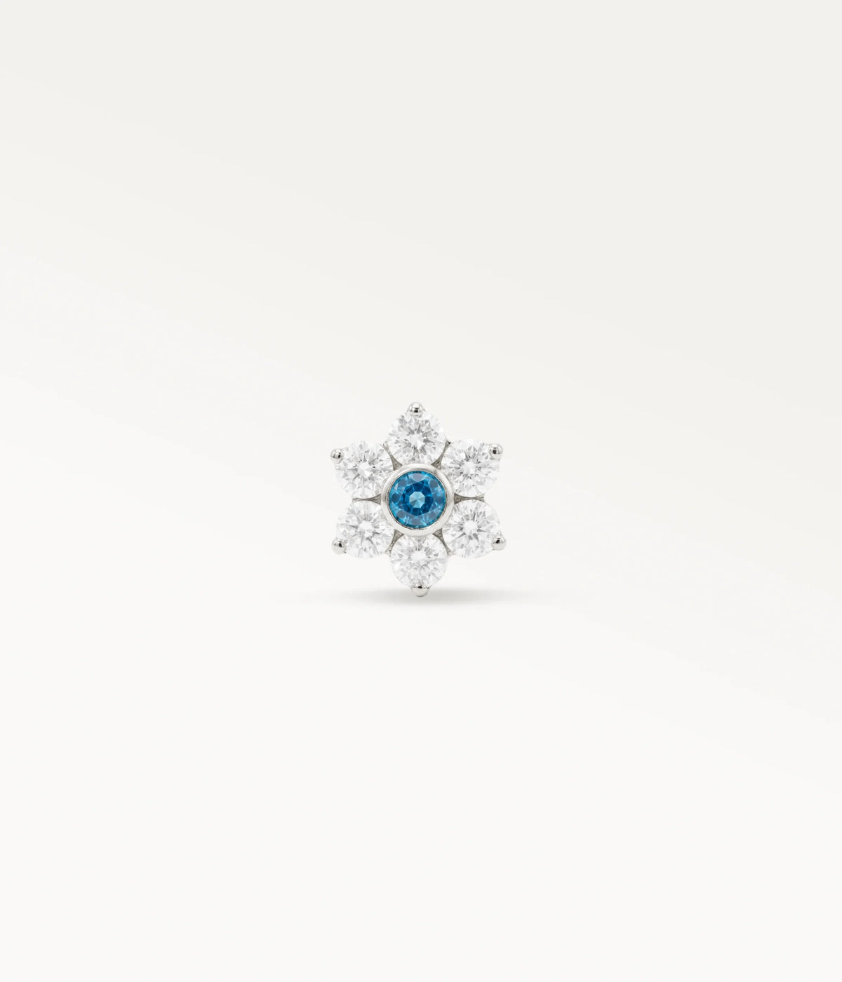 Vista frontal de un piercing de oreja color plateado adornado con una flor con piedra azul central y circonitas.