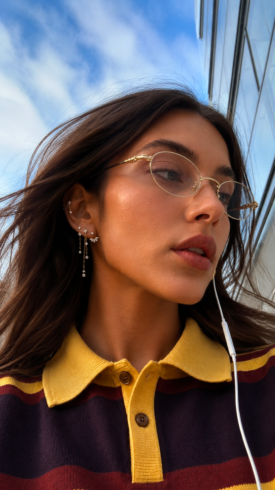 Portrait en extérieur avec lunettes et fines chaînes suspendues aux bijoux d’oreille.