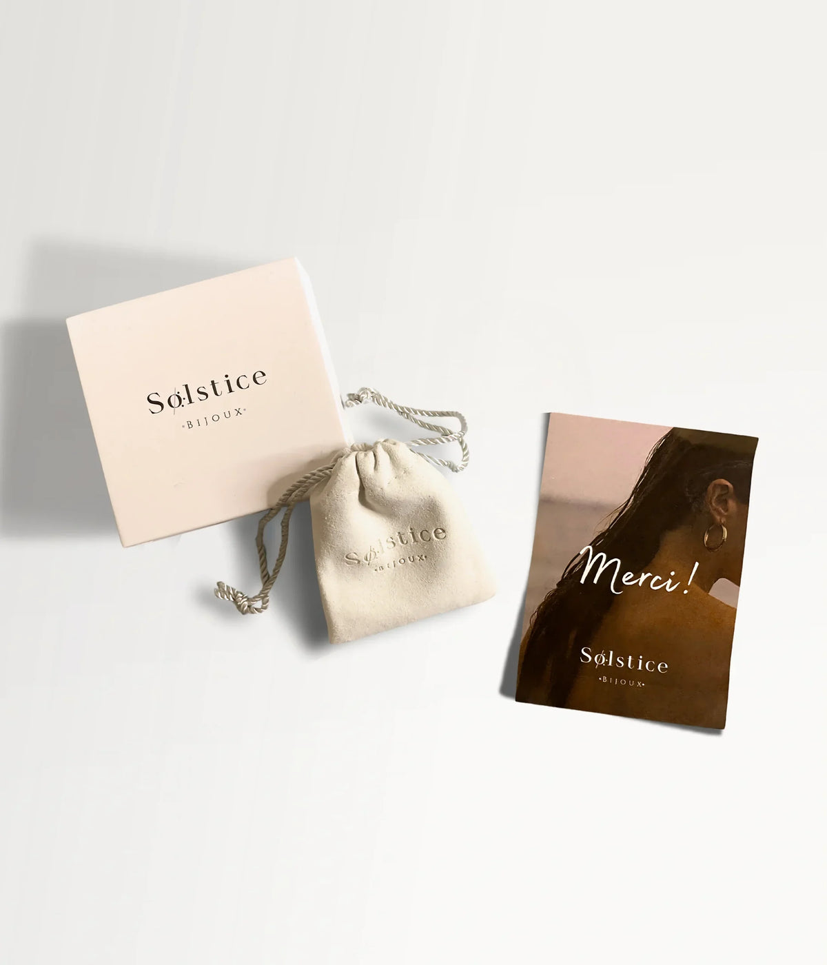 Rosafarbene Solstice-Box, Beutel mit Zugband und Karte „Merci“.