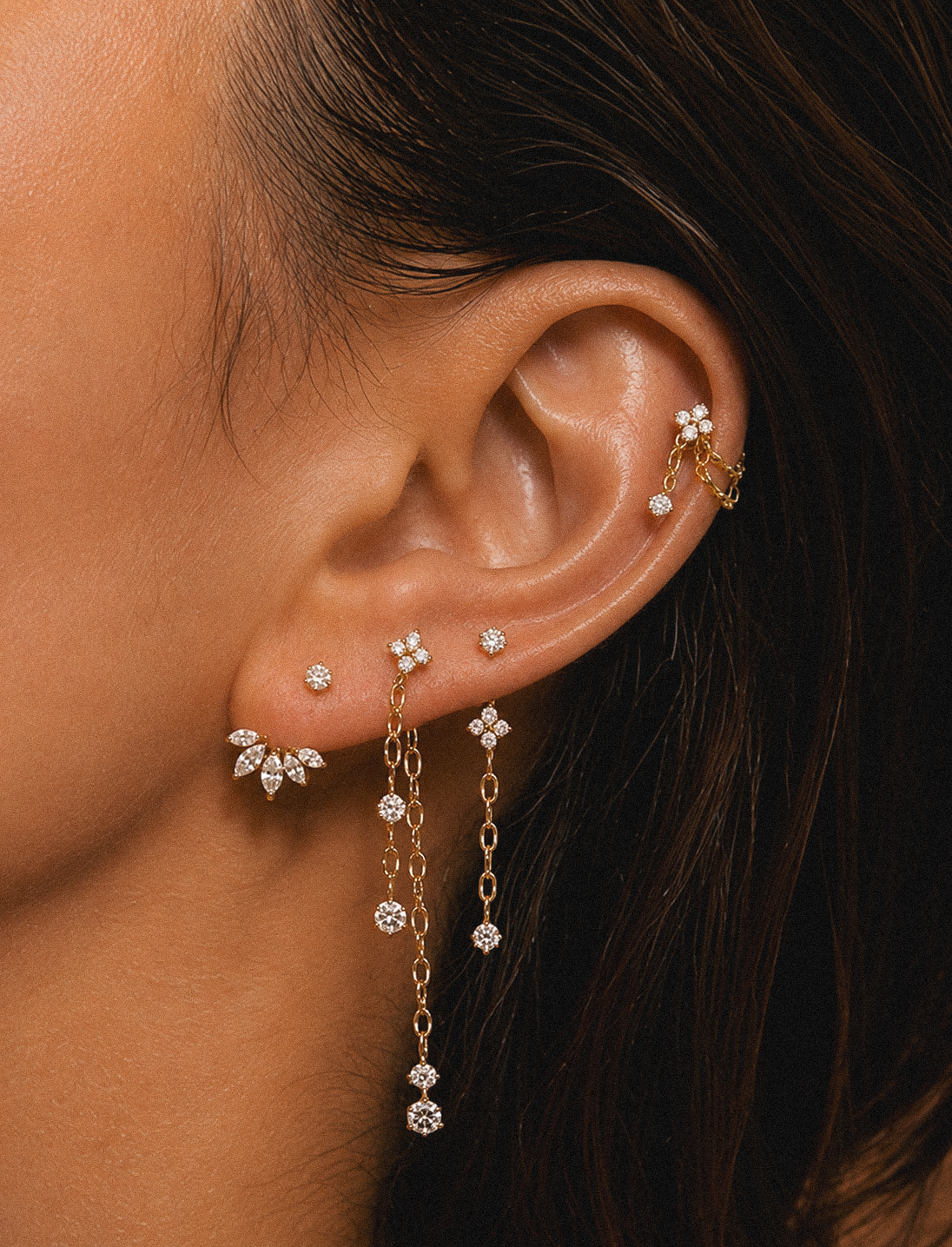 Gros plan sur trois chaînes dorées au lobe, accompagnées de bijoux à pierres.