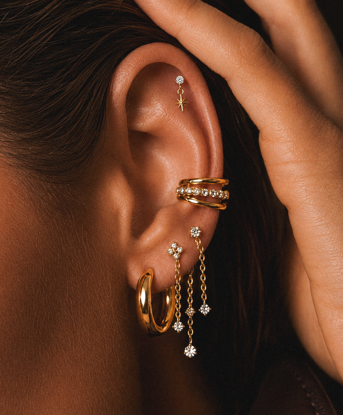 Gros plan sur une oreille avec triple anneau au conch et chaînes pendantes au lobe.