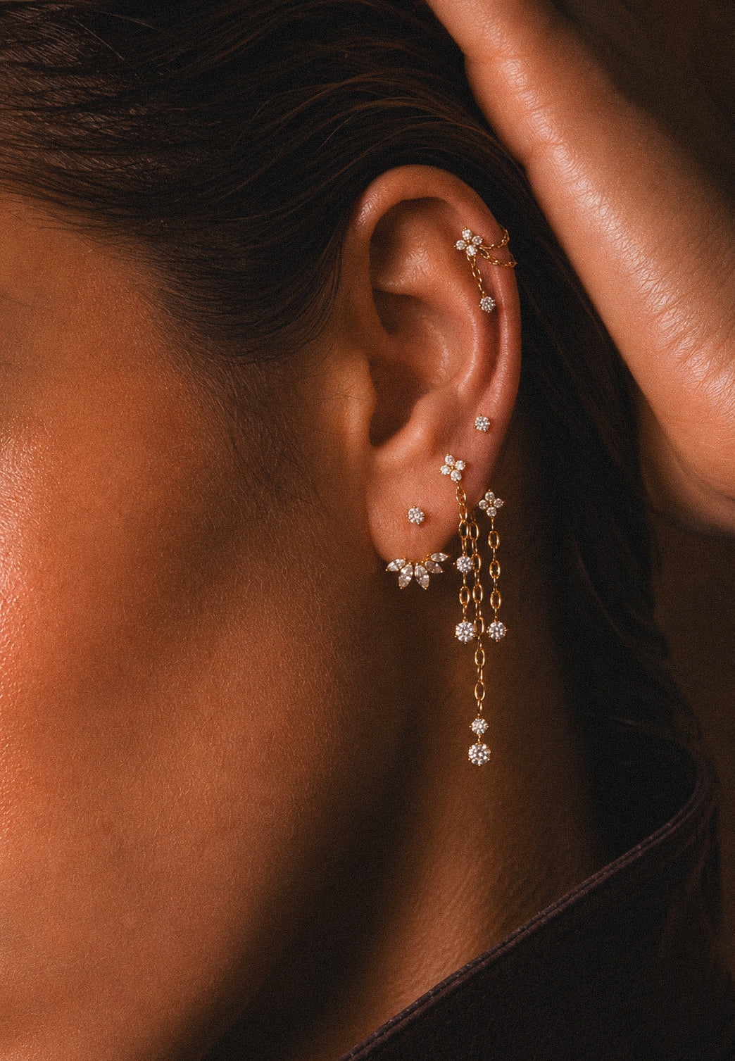 Oreille ornée de bijoux à pierres au lobe, de chaînes pendantes et d’une fleur à l’hélix.