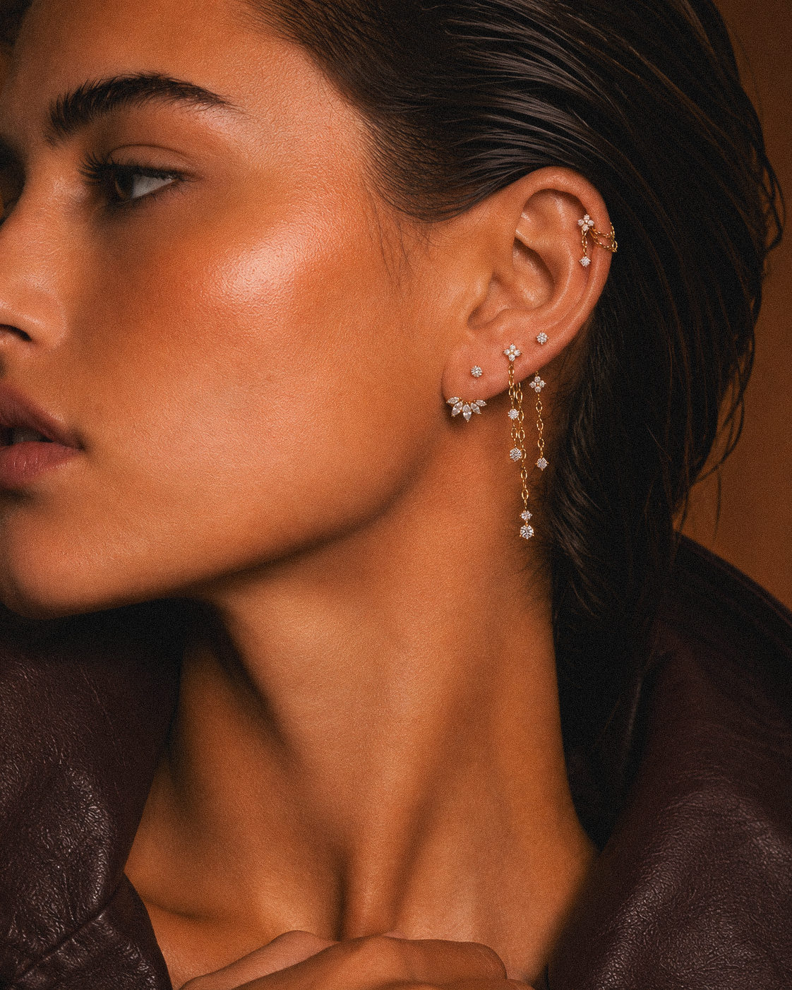 Portrait de profil avec bijoux à pierres et chaînes dorées portées au lobe.