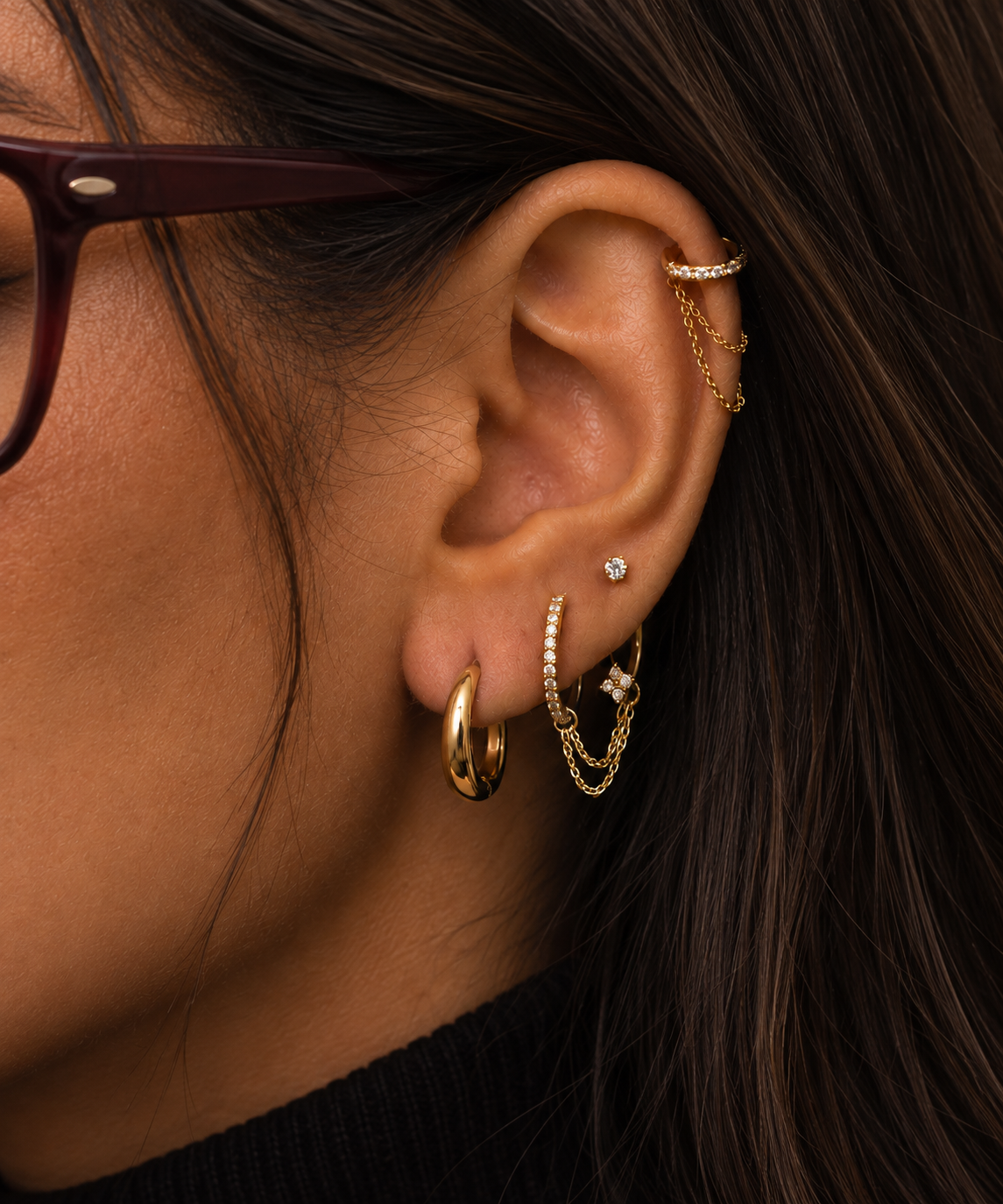 Gros plan sur une oreille ornée de créoles à chaîne au lobe et d’un anneau à l’hélix.