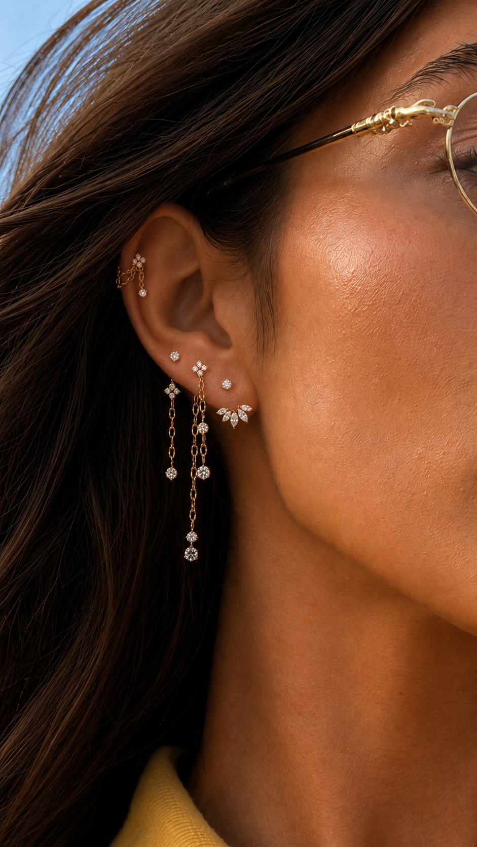 Gros plan sur une oreille ornée de pierres au lobe et de plusieurs chaînes dorées pendantes.