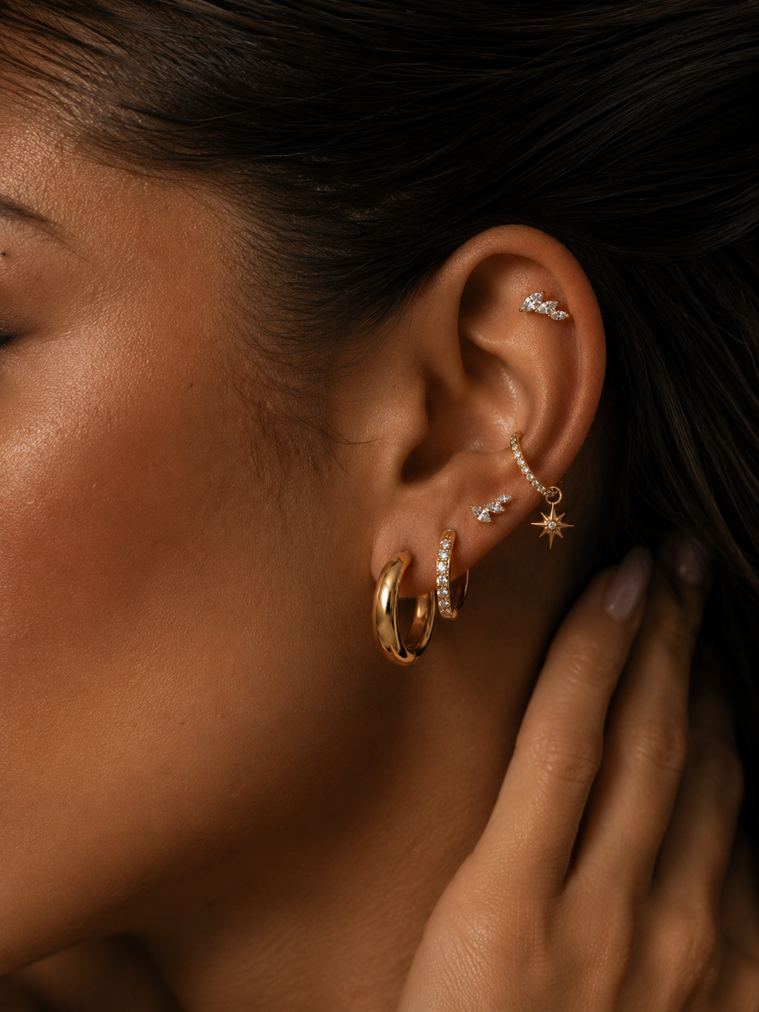Oreille ornée de créoles dorées et de pierres marquise au lobe et à l’hélix.