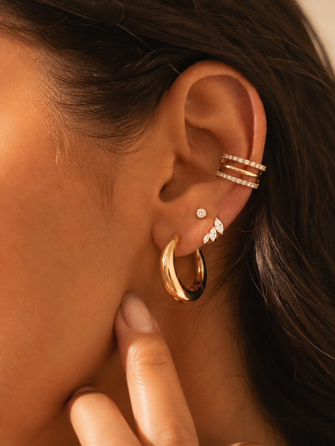 Gold-tone ear stack being worn with a large hoop and stones on the lobe, and a triple hoop at the conch.