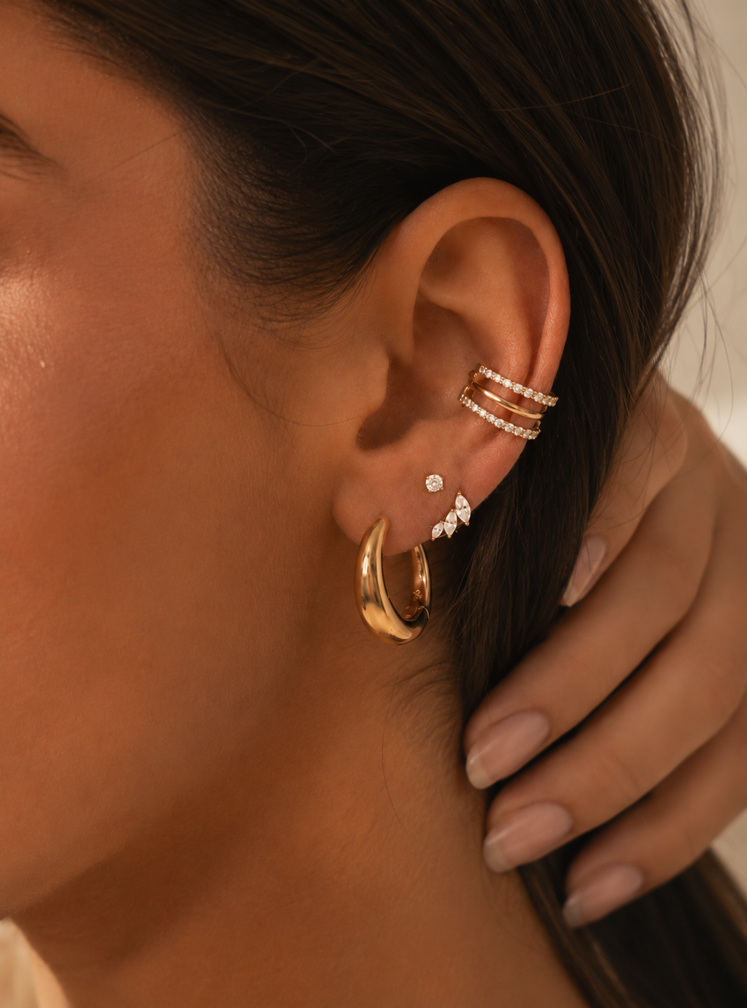 Ilies ear stack being worn, with a large gold-tone hoop on the lobe and a triple hoop at the conch.
