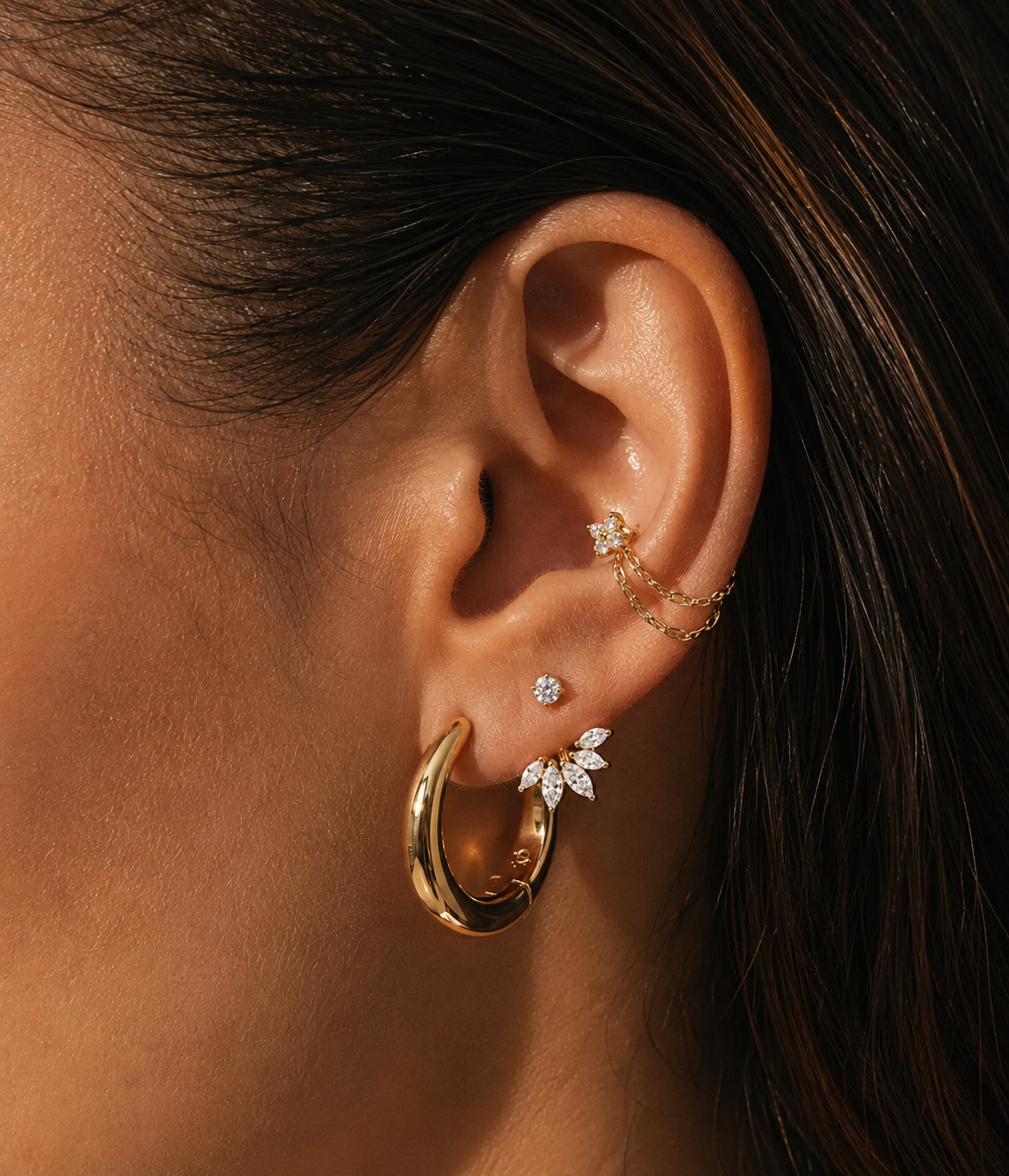 Goldfarbene Doppelkette am Conch, kombiniert mit breiter Creole und Steinen am Ohrläppchen.