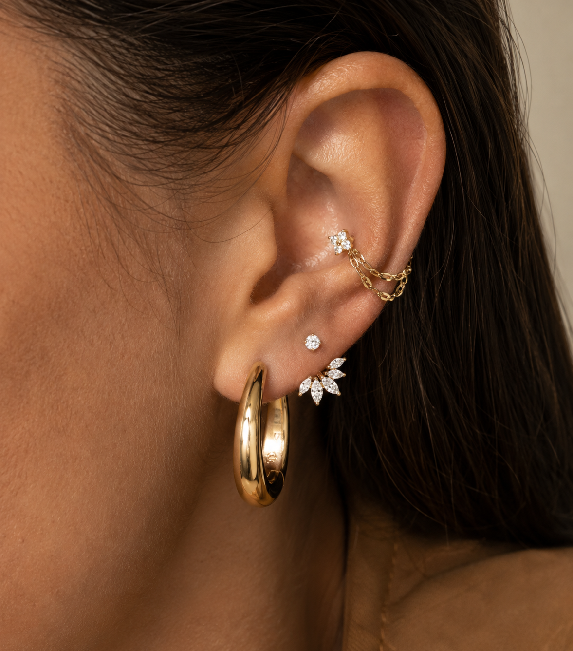Double gold-tone chain worn around the conch with a wide hoop and stones on the lobe.