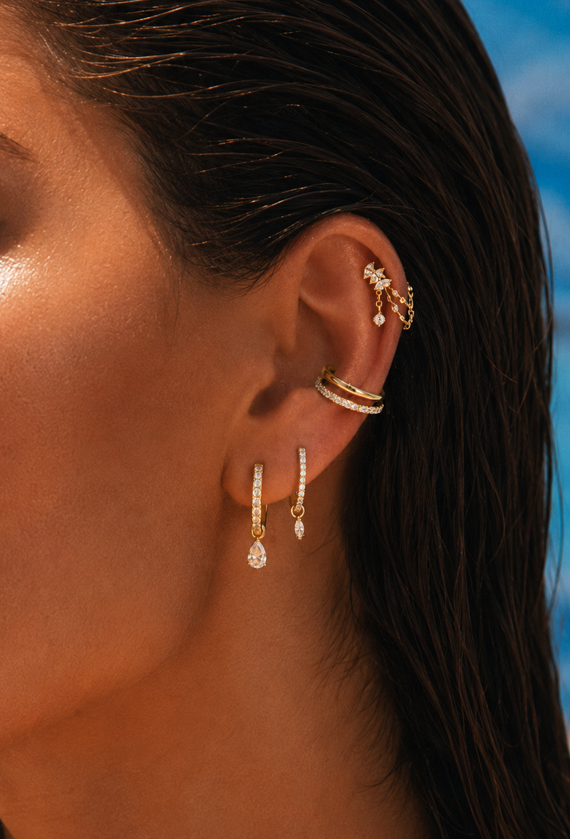 Oreille ornée de créoles à pendentifs, d’un double anneau au conch et de pierres à l’hélix.