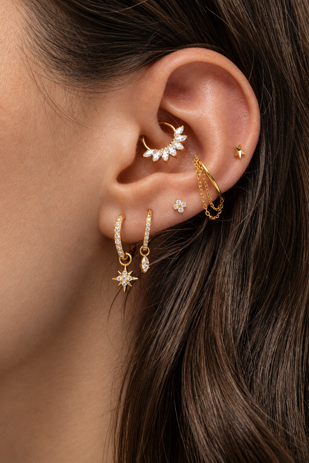 Oreille ornée de bijoux dorés, avec pendentif étoile au lobe et anneau à pierres au daith.