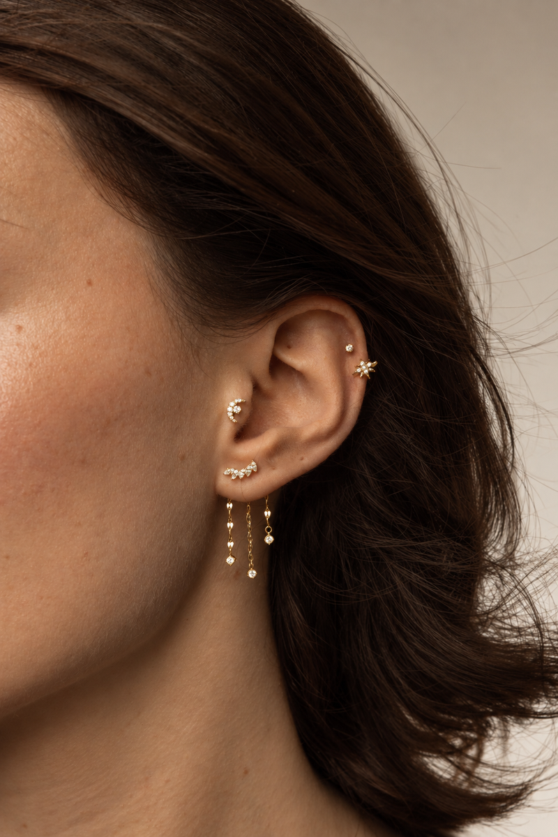 Bijoux dorés portés avec lune au conch, pierres au lobe et fines chaînes pendantes.